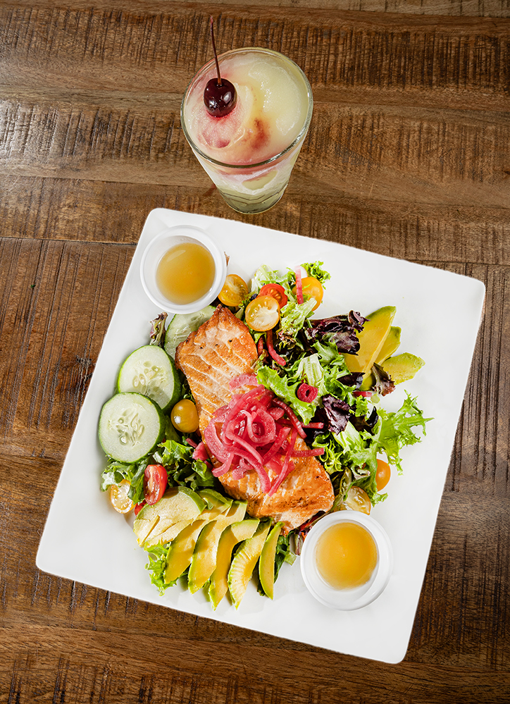 salmon salad with vegetables in a square plate on a wood table with a frozen drink on the side